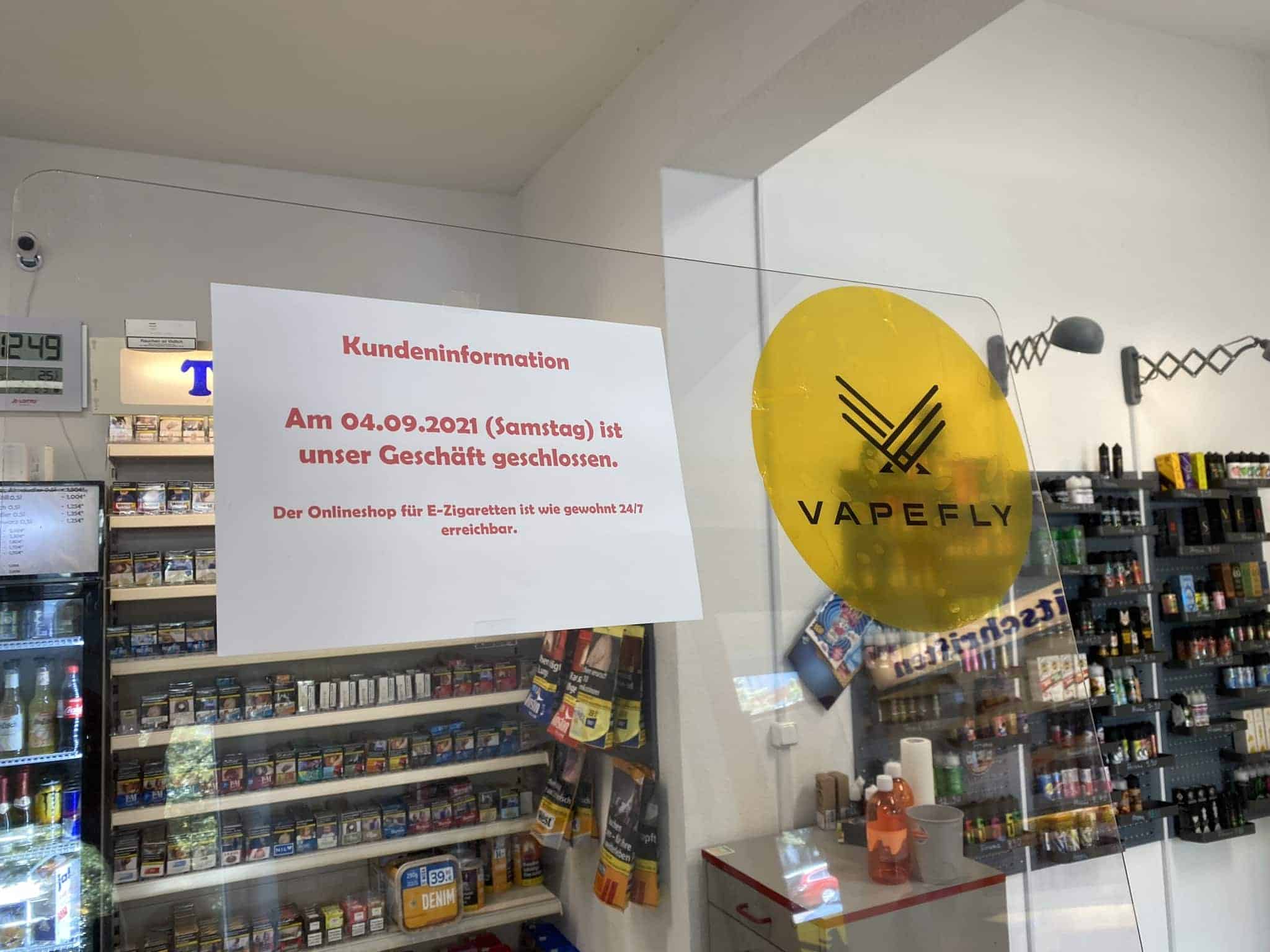 VapeFly Logo an einer Glaswand im Tabakshop, reflektiert bei Tageslicht, mit schwarzem und gelbem Design, Hinweis auf Geschäftsschließung am 04.09.2021.